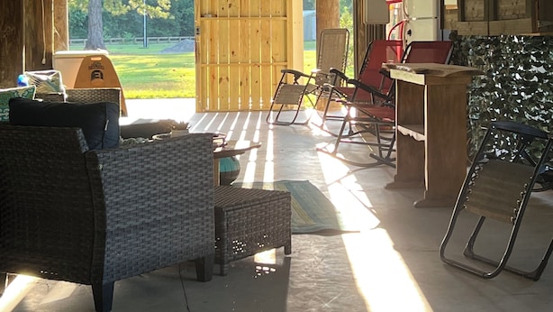 A covered outdoor area with a ceiling fan, wooden walls, a wooden door, a refrigerator, a table, and a chair.