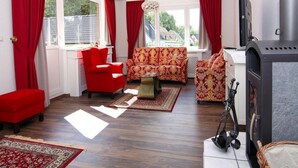 A living room with a red sofa, patterned armchairs, a glass coffee table, and a fireplace.
