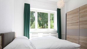 A bedroom with a bed, a window with curtains, a wooden wardrobe, and a pendant light.