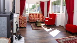 A cozy living room with a fireplace, red and patterned sofas, and a large window with curtains.