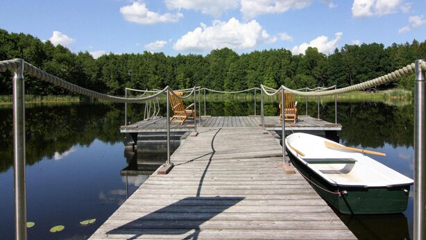 A wooden dock extending into calm water with two chairs and a boat moored at the end.