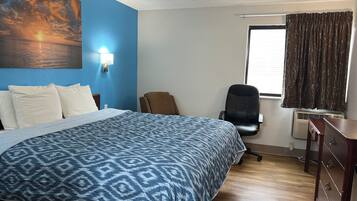 A hotel room with a bed, a desk, a chair, a window with curtains, and a wall with a painting.