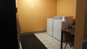 A laundry room with a washing machine and dryer, a small table, and a chair. - Extended Stay Warrenton Inn (Warrenton)