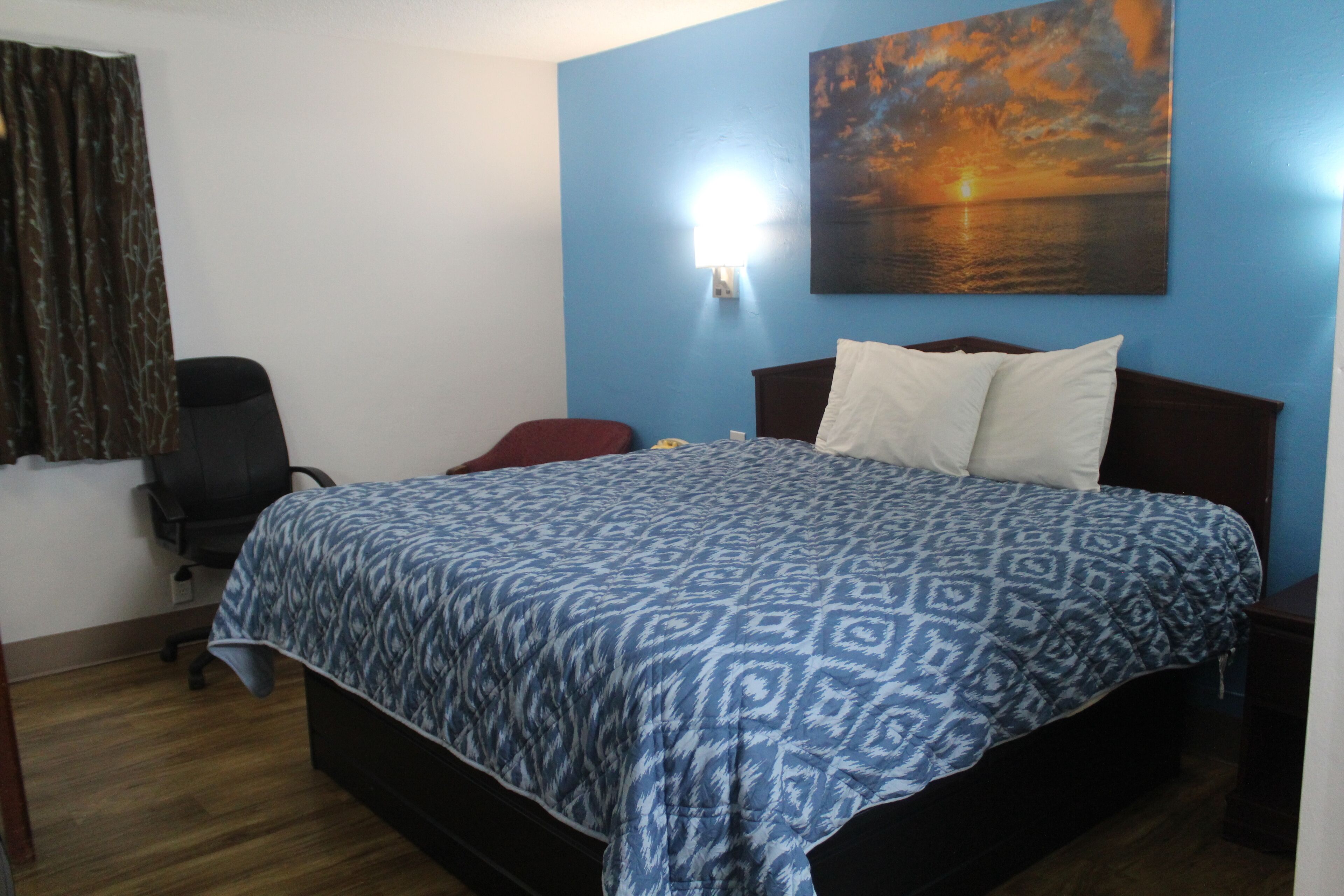 A bedroom with a bed, a chair, a desk, and a painting on the wall.