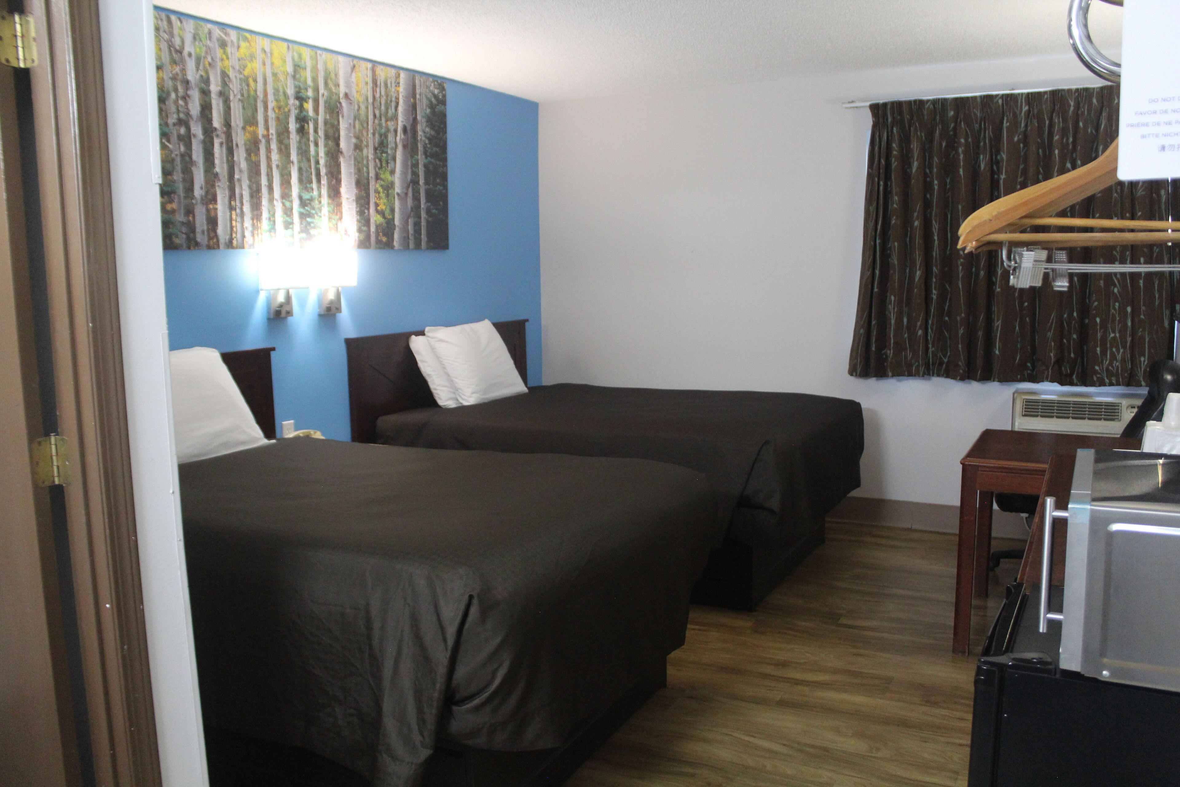 Habitación de hotel con dos camas, un escritorio de madera, un equipo de aire acondicionado y un cuadro en la pared.
