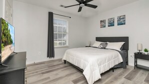 Ein Schlafzimmer mit einem Bett, einem Deckenventilator, einem Fernseher, einem Fenster mit Vorhängen und Bildern an der Wand.