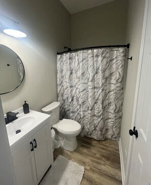 A bathroom with a white toilet, a sink with a mirror, and a marble-patterned shower curtain. - Charming 1-bedroom fish shack in Somerset with WiFi and AC (Somerset)