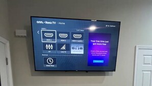 Een flatscreen televisie aan een muur, waarop het Roku TV Home menu wordt weergegeven.