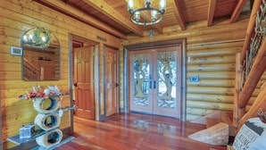 L’intérieur d’une cabane en rondins, avec des murs et un plancher en bois, un lustre et une porte ornée d’un motif représentant un arbre.