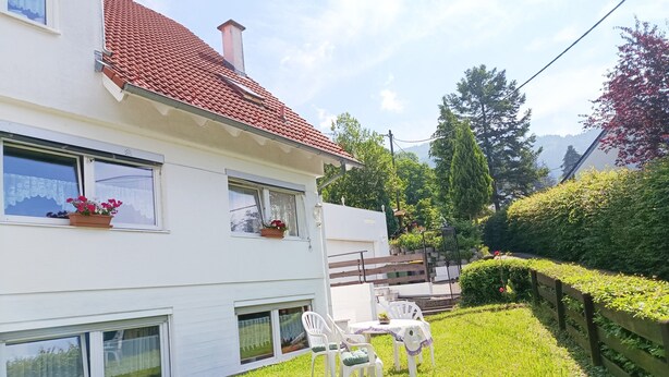 Une maison blanche avec un toit recouvert de tuiles rouges, un petit jardin avec une table et des chaises, et une clôture en bois.