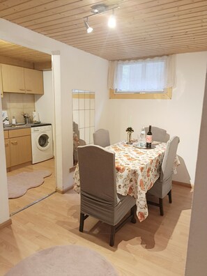 Un coin repas avec une table dressée pour deux personnes, un lave-linge en arrière-plan et une fenêtre donnant sur un paysage agréable.