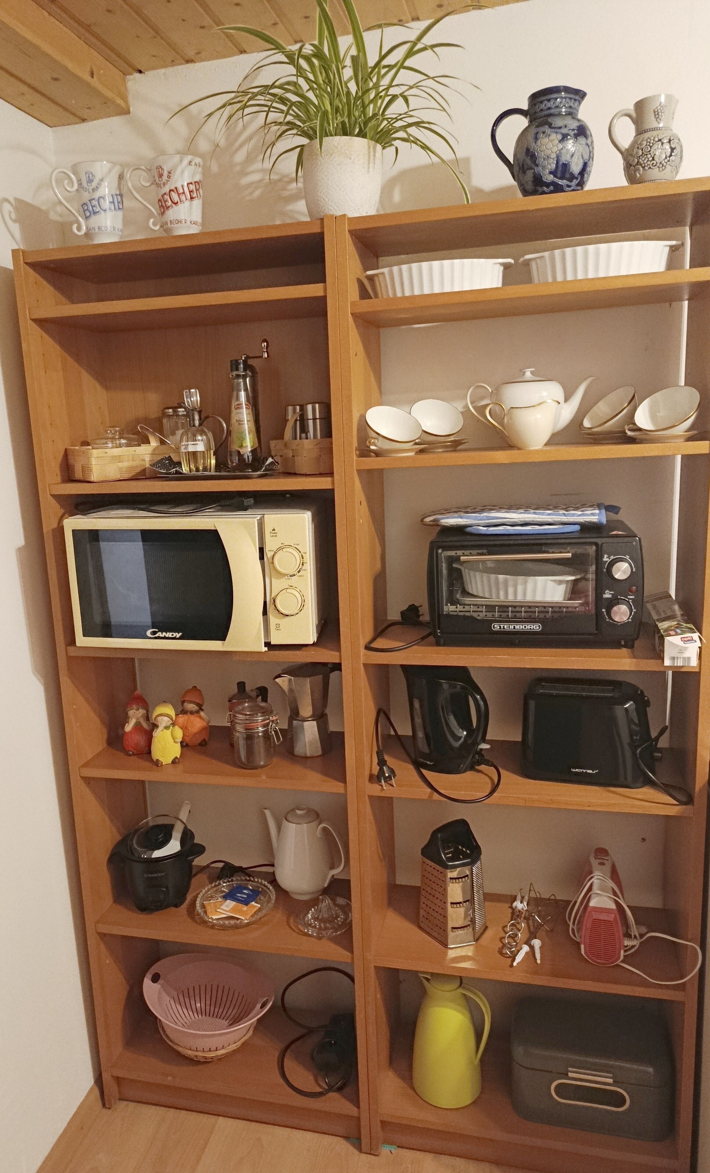 A kitchen with wooden shelves, a microwave, a toaster, and various kitchen utensils.