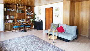 Un salon spacieux avec un haut plafond, des étagères en bois, un canapé, un coin repas et un lustre.