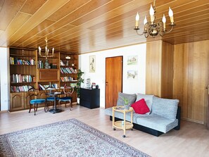 Ein geräumiges Wohnzimmer mit hohen Decken, Holzregalen, einer Couch, einem Essbereich und einer Chandelier.