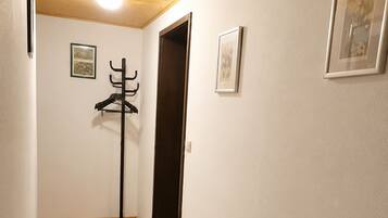 Un couloir doté d’un plancher en bois, de deux tapis à motifs gris, d’un porte-manteau et de tableaux encadrés accrochés aux murs.