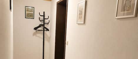 A hallway with wooden flooring, two grey patterned rugs, a coat rack, and framed pictures on the walls.