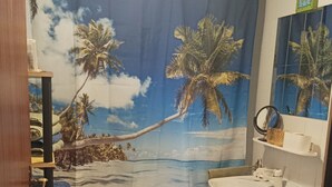 A bathroom with a shower curtain depicting a beach scene, a sink, a toilet, and a green mat. - Vacation apartment Erika (Badenweiler)