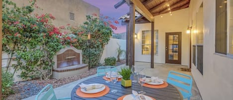 An outdoor patio with a round table set for dining, surrounded by chairs, and a built-in barbecue grill.