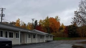 A parking lot with a row of motel-style buildings, a black truck, and autumn-colored trees in the background. - Fundy Line Motel (Miramichi)
