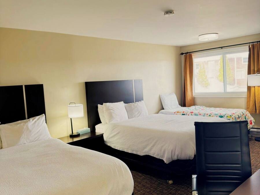 Habitación de hotel con dos camas, un escritorio, una silla y una ventana con cortinas.