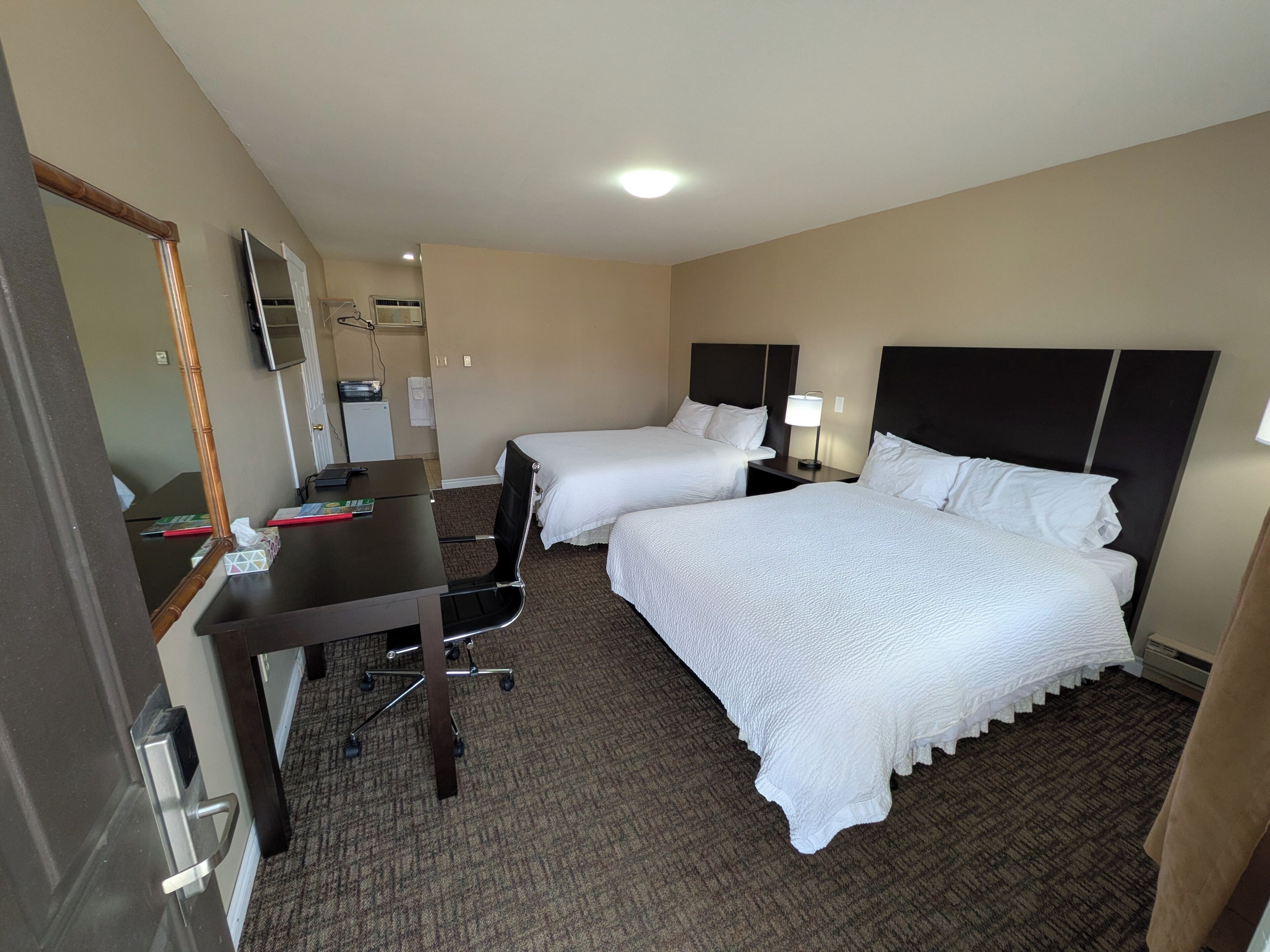 Habitación de hotel con dos camas, un escritorio, una silla, un televisor y un espejo.