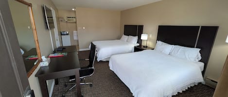 Habitación de hotel con dos camas, un escritorio, una silla, un televisor y un espejo.