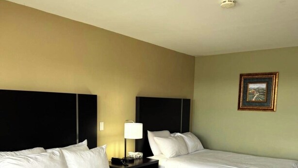 A hotel room with two beds, a nightstand with a lamp, and a framed picture on the wall. - Fundy Line Motel (Miramichi)