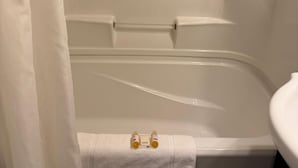 A bathroom with a bathtub, a white towel, and two bottles on the towel. - Fundy Line Motel (Miramichi)
