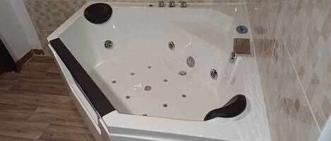Un baño con una bañera blanca, paredes con azulejos y suelo de madera.