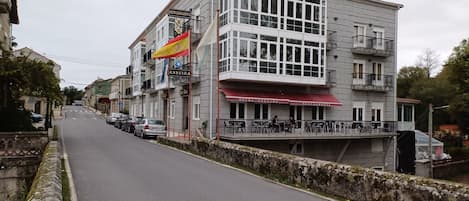 Un edificio con letreros de restaurante y hotel, un balcón con sillas y un muro de piedra a lo largo de la calle.