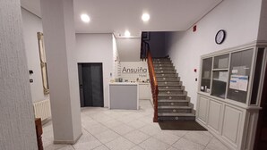 Un vestíbulo de hotel con una escalera, una recepción y un reloj en la pared.