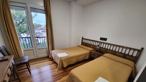 Habitación de hotel con dos camas individuales, un escritorio de madera, una silla y una ventana con cortinas.