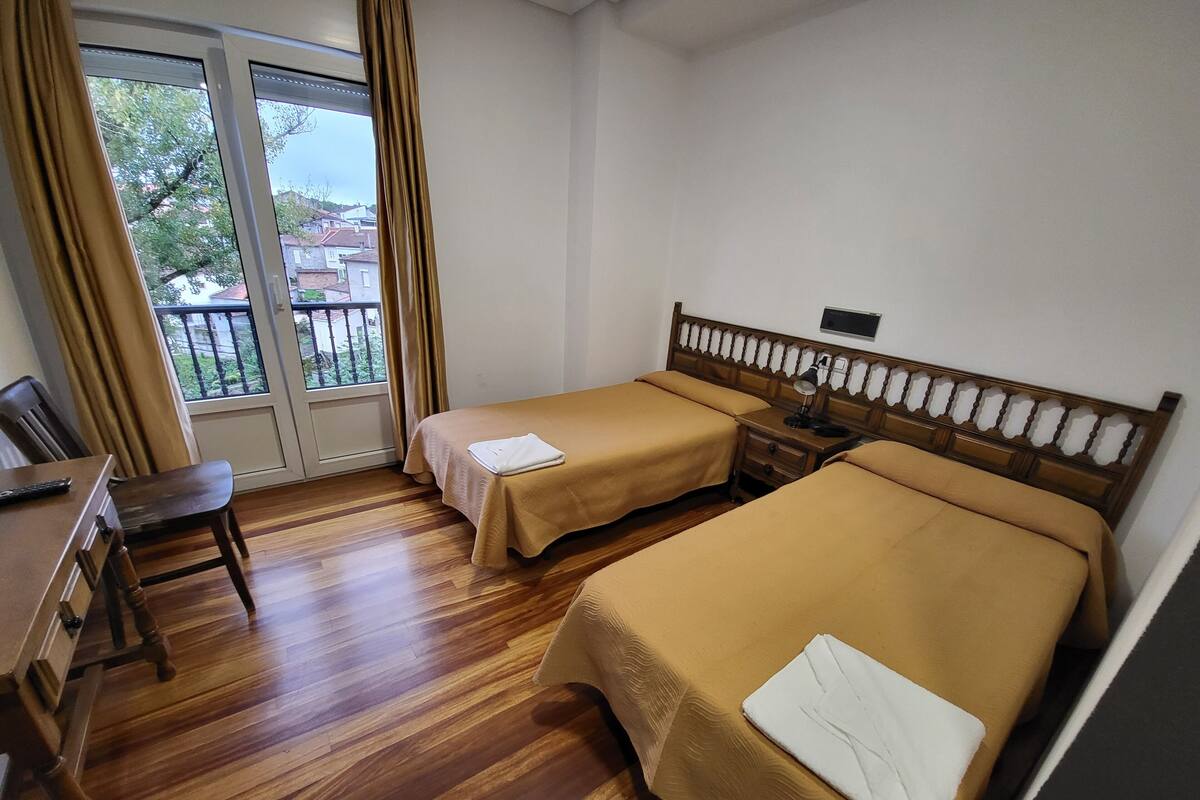 A hotel room with two single beds, a wooden desk, a chair, and a window with curtains.