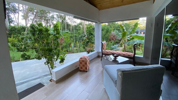 A covered patio with a view of a garden, a cushioned bench, and a sofa.