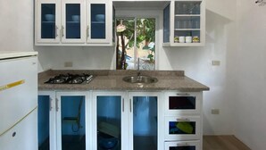 A compact kitchen with white cabinets, a gas stove, and a window overlooking greenery.