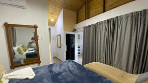 A room with a bed, a sofa, a mirror, and a window with curtains.