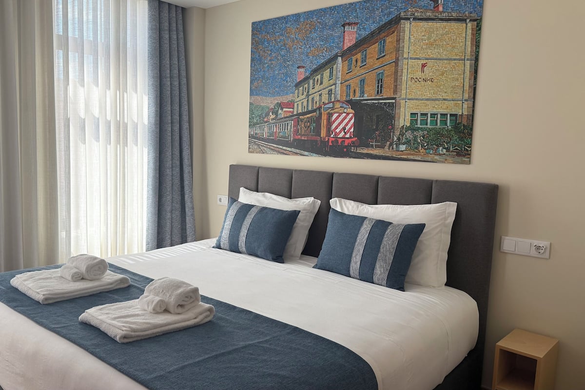 A hotel room with a large bed, two pillows, a blue blanket, and two towels.