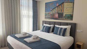 A hotel room with a large bed, two pillows, a blue blanket, and two towels.