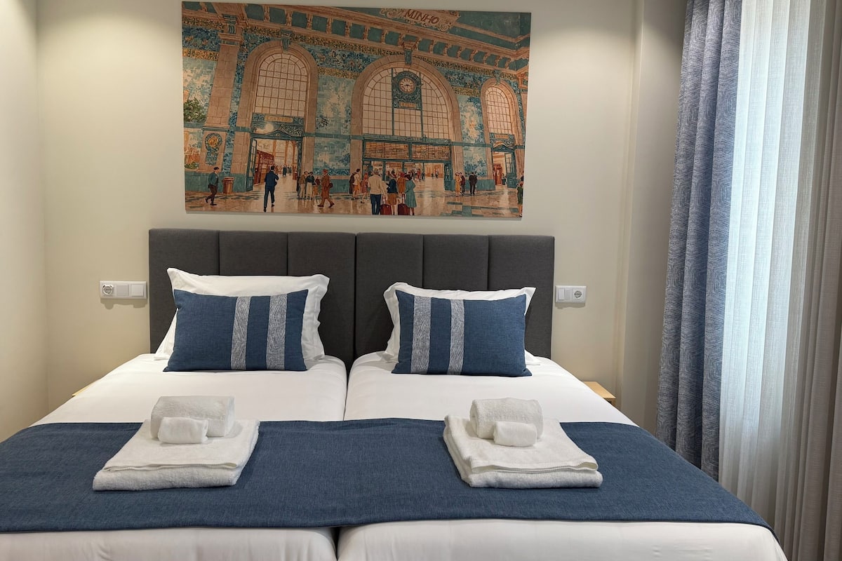A hotel room with a large bed, two pillows, a headboard, and a painting above the bed.