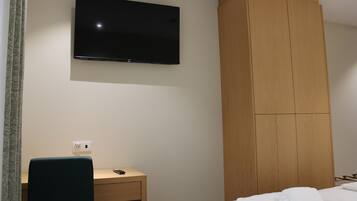 A hotel room with a bed, a desk, a television mounted on the wall, and a wooden wardrobe.