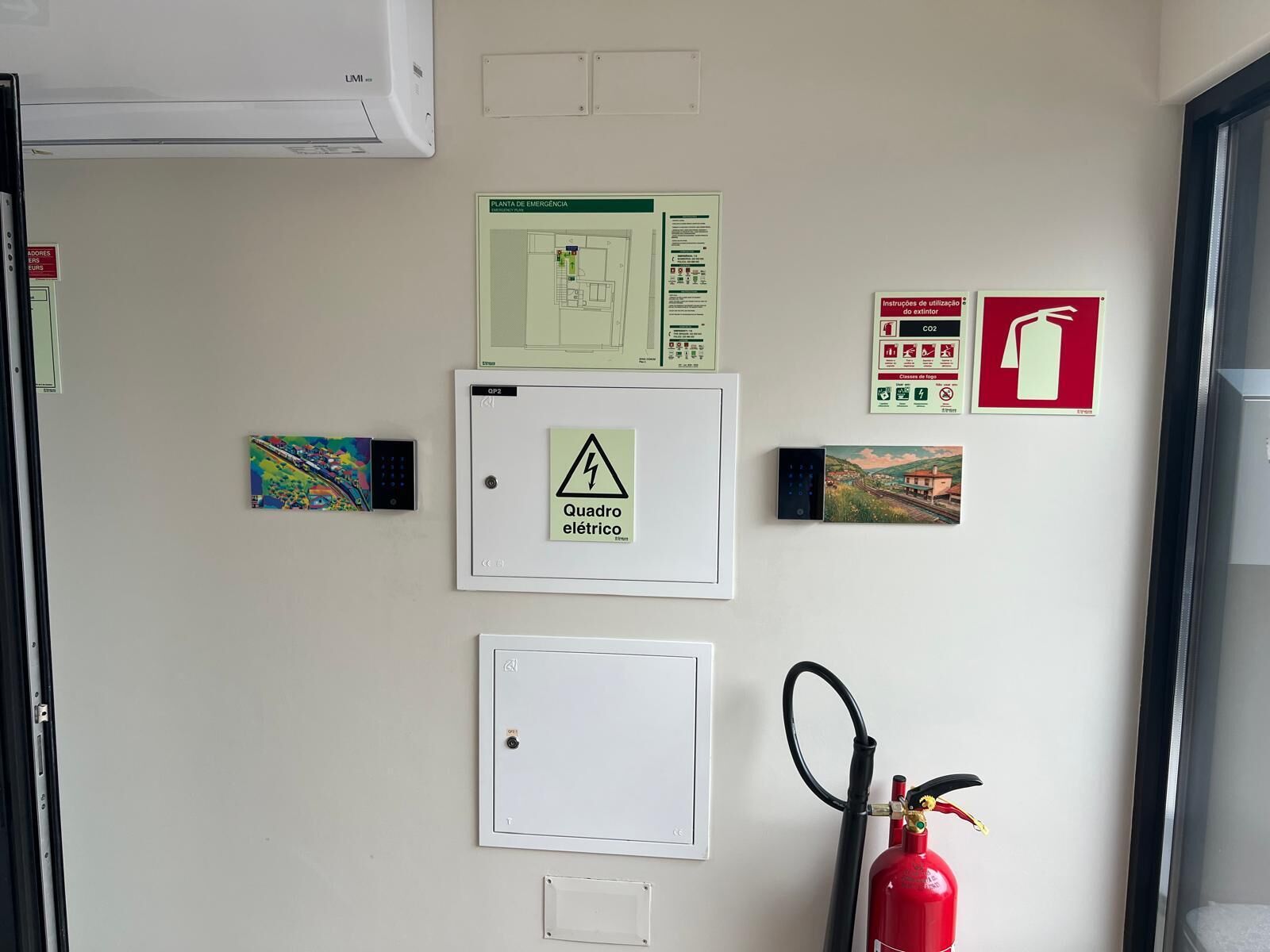 A wall with emergency instructions, a fire extinguisher, and electrical panel covers.