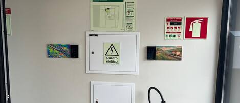 A wall with emergency instructions, a fire extinguisher, and electrical panel covers.