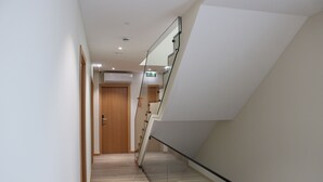 Ein modernes Interieur mit einer Holztür am Ende eines Ganges, einer Glastrennwand an einer Treppe und einem hellen Boden.