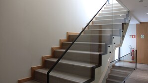 Eine moderne Treppe mit Holzboden und Glasgeländern, die zu einer Zwischenebene mit einem Feuerlöscher und einer Tür führt.