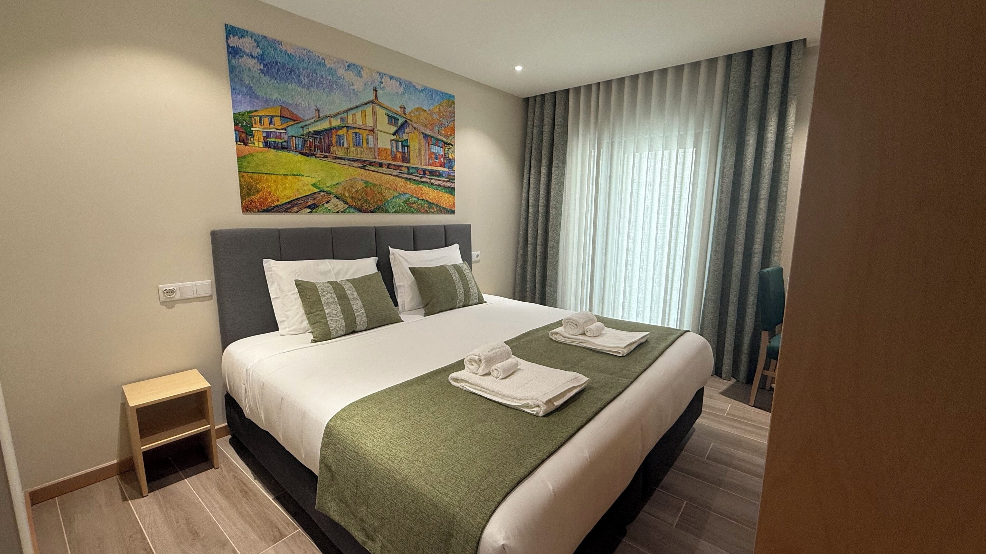 Une chambre d’hôtel avec un grand lit, un tableau au mur et une vue sur l’extérieur par la fenêtre.