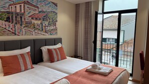 Ein Hotelzimmer mit zwei Betten, einem großen Fenster mit Blick auf Gebäude und einem farbenfrohen Wandgemälde.