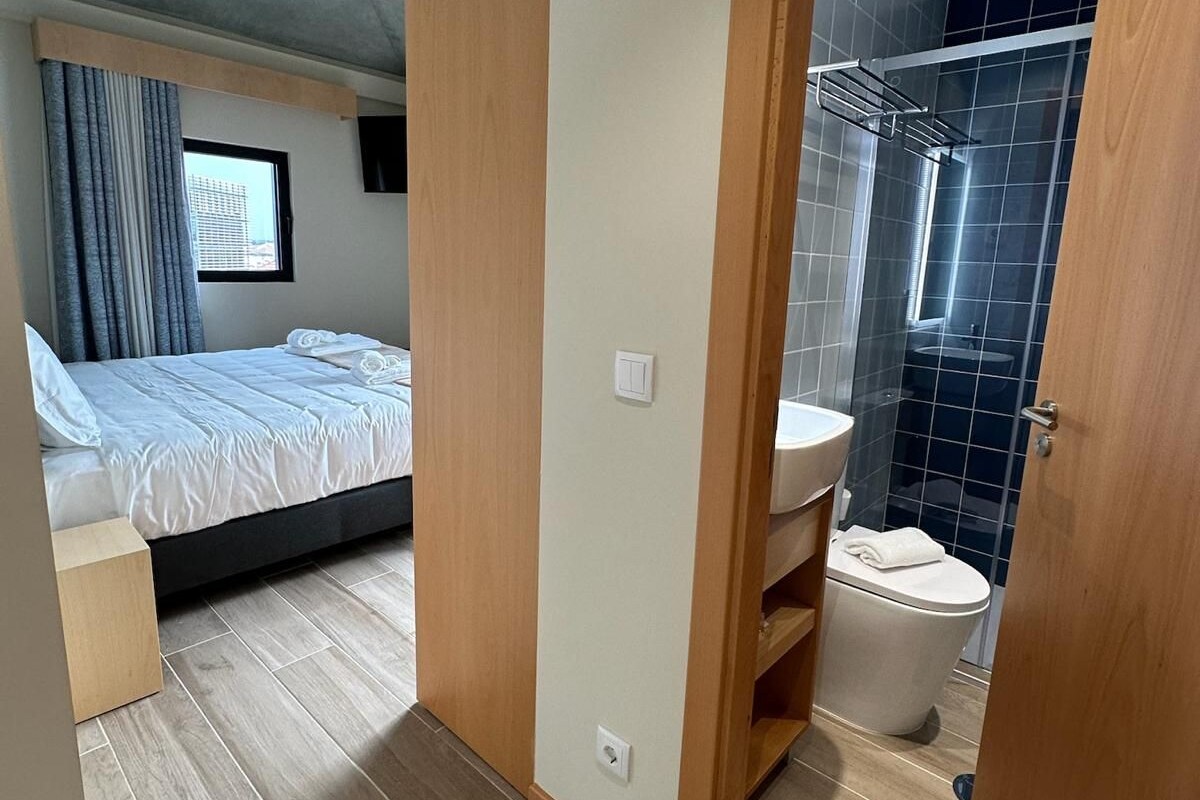 Een moderne slaapkamer met een bed, een houten kledingkast en een badkamer met douche en toilet.