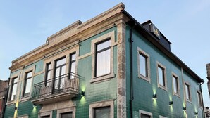 Ein zweistöckiges Gebäude mit grünen Fliesenwänden, zahlreichen Fenstern und einem Balkon mit Metallgeländer.