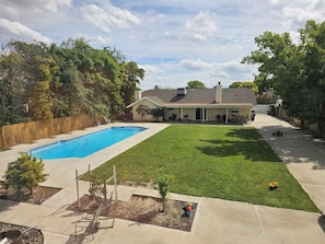 Un patio trasero residencial con piscina, césped y zona de patio.