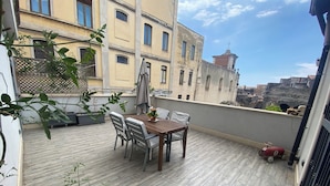 A wooden deck with a table and chairs, potted plants, and a red toy car. - The Odeon Terrace (Catania)